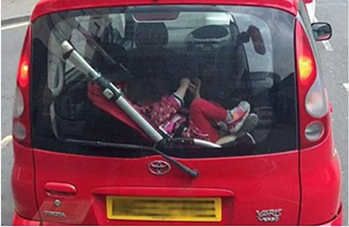 child strapped into pushchair in car boot